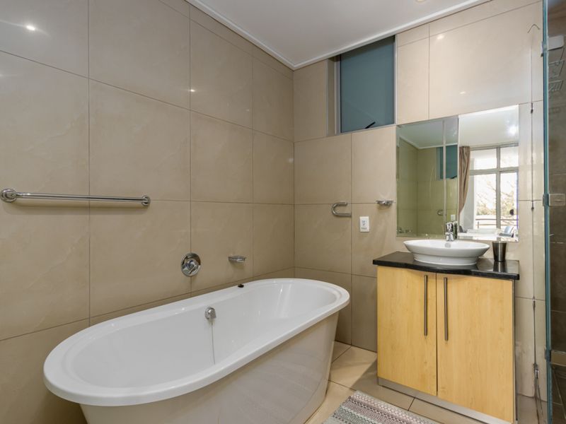 Modern bathroom featuring a freestanding bathtub, a vanity with a vessel sink, and a glass-enclosed shower with neutral wall tiling.