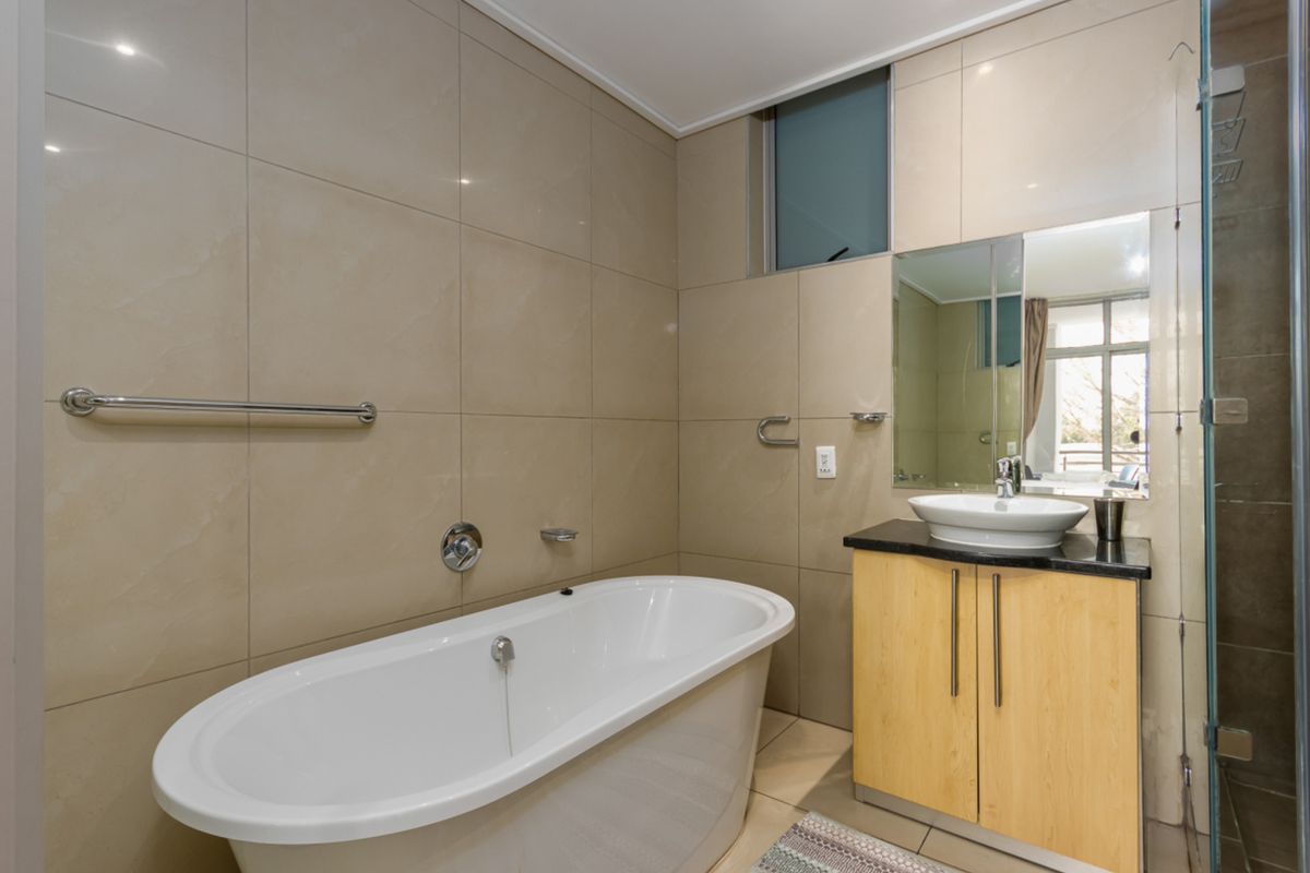 Modern bathroom featuring a freestanding bathtub, a vanity with a vessel sink, and a glass-enclosed shower with neutral wall tiling.