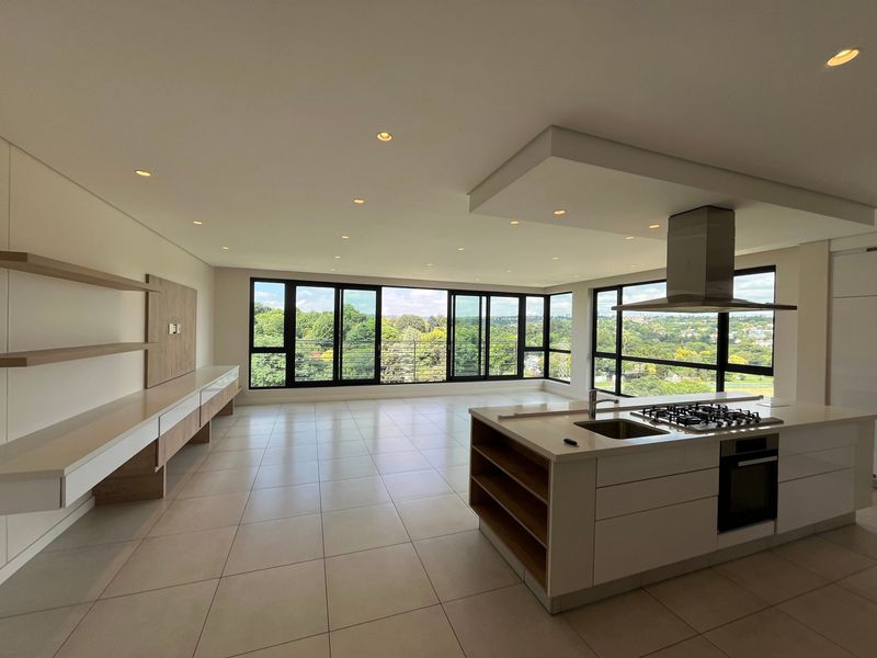 Spacious open-plan living and kitchen area featuring a modern island with gas hob, sleek cabinetry, and expansive windows offering panoramic views.
