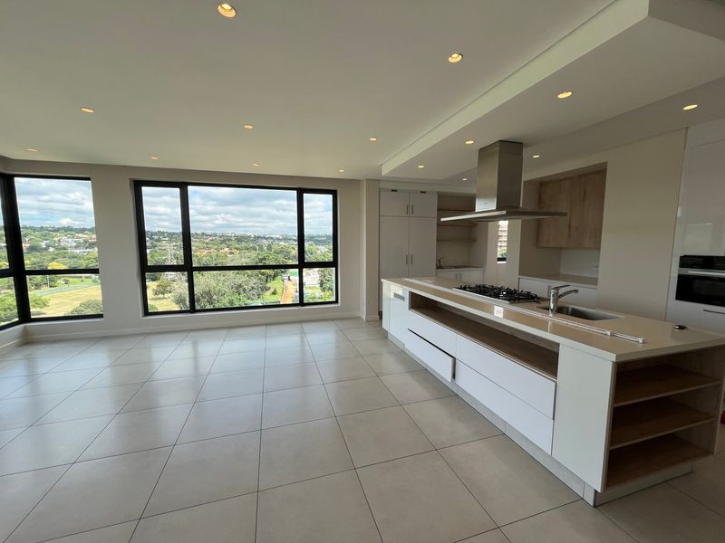 Modern open-plan kitchen and living area featuring a large island with gas hob, sleek cabinetry, and expansive windows offering panoramic views.