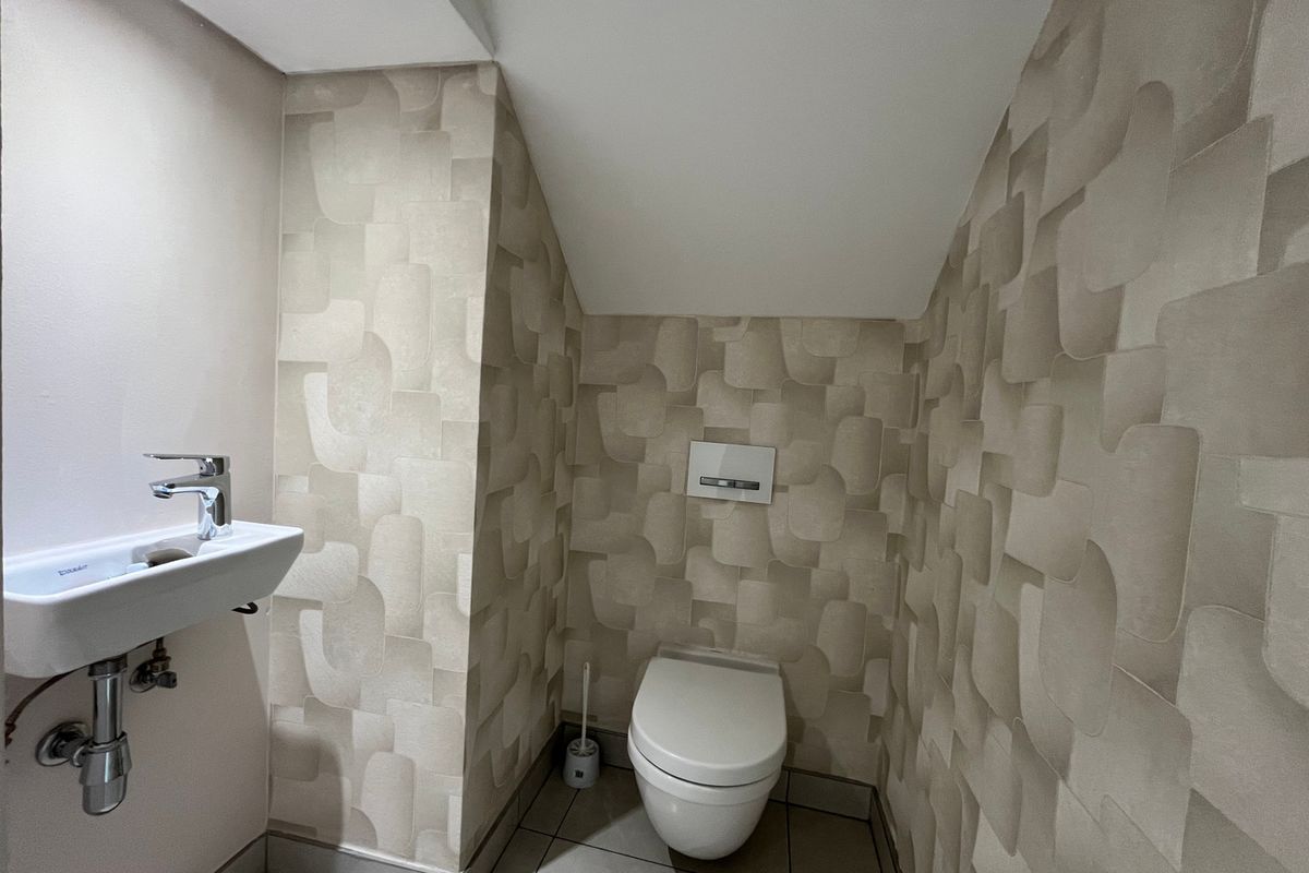 A compact, modern guest bathroom featuring a wall-mounted toilet with a concealed cistern, a sleek wall-mounted basin, and contemporary patterned wallpaper.