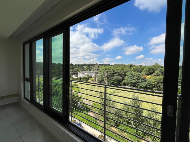 A clean, modern balcony featuring large sliding glass doors and a metal balustrade, offering an expansive view of the surrounding green landscape.