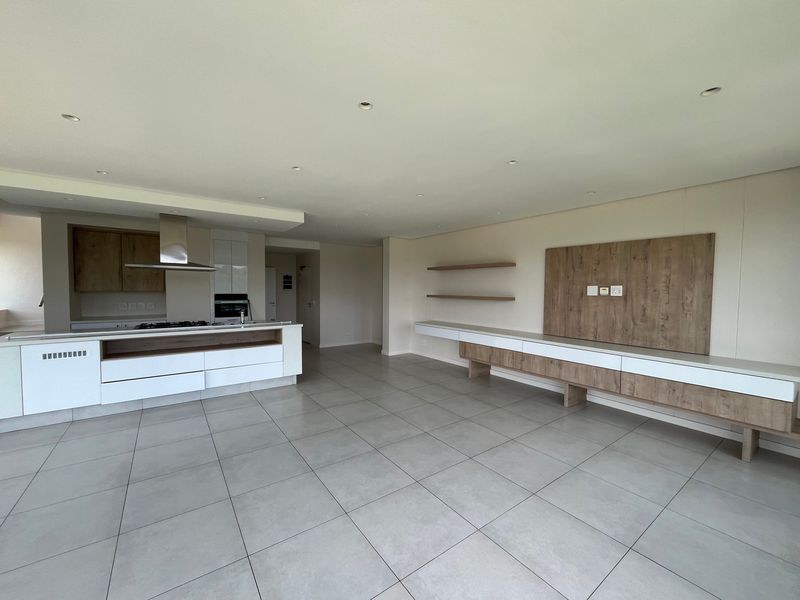 Spacious open-plan living area featuring a modern kitchen with built-in appliances and a custom media console with floating shelving.