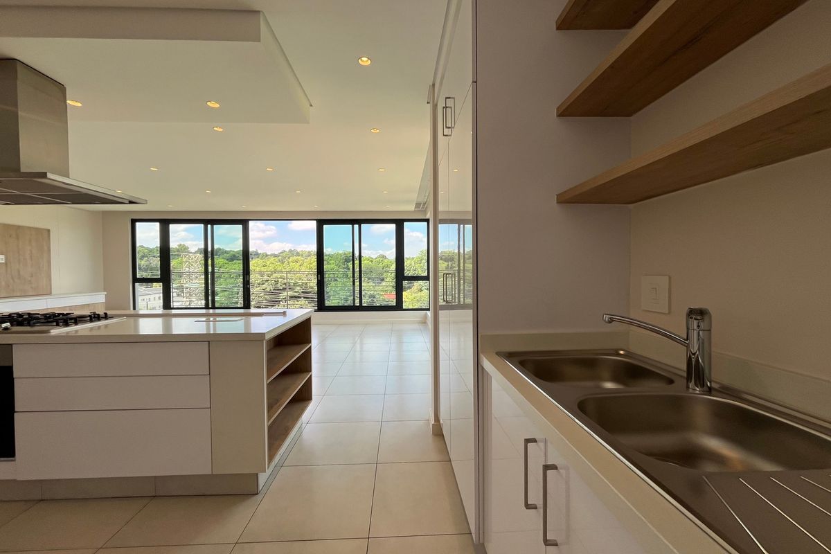 Modern open-plan kitchen and living area featuring a central island, sleek cabinetry, high-end finishes, and large sliding doors with expansive views.