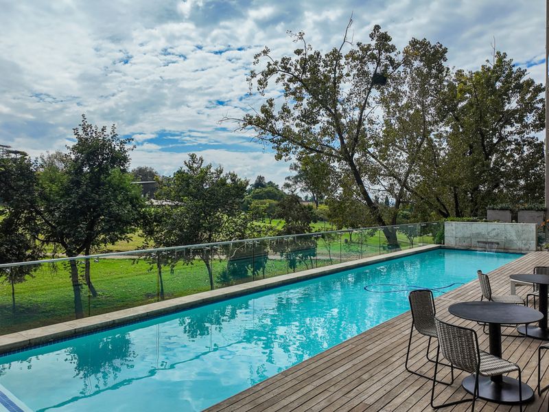 A modern swimming pool area featuring timber decking, a glass balustrade, and a scenic view of the surrounding greenery.