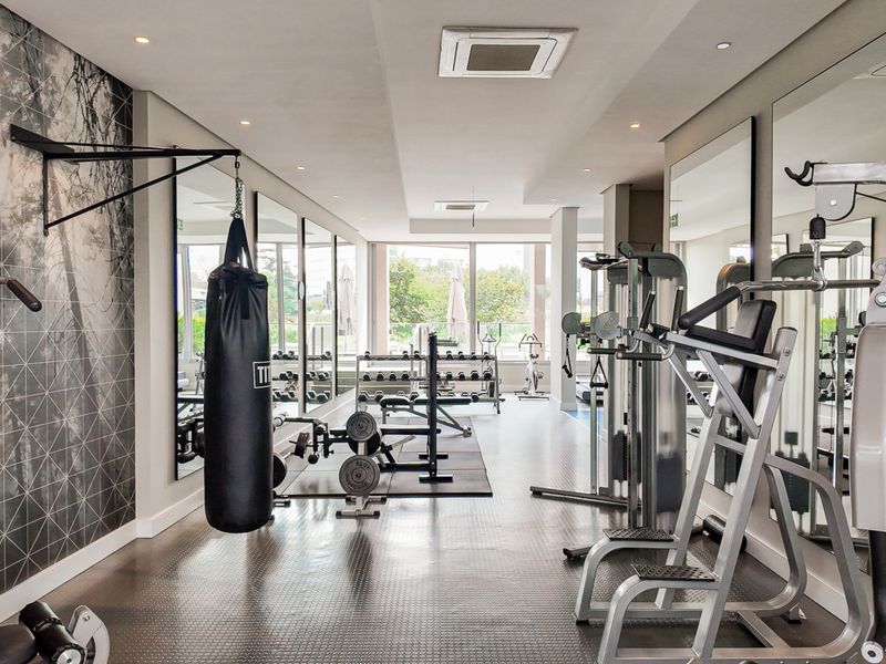 A well-maintained, modern residential gym featuring mirrored walls, durable rubberized flooring, and integrated ceiling lighting and air conditioning.