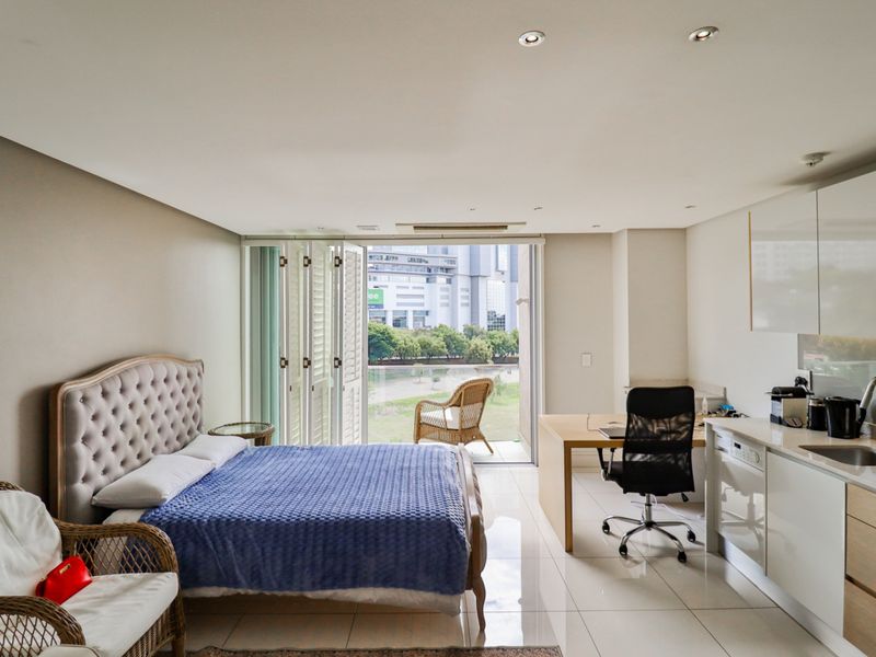 Modern open-plan studio apartment featuring a kitchenette, tiled flooring, recessed lighting, and folding glass doors opening to a balcony with urban views.