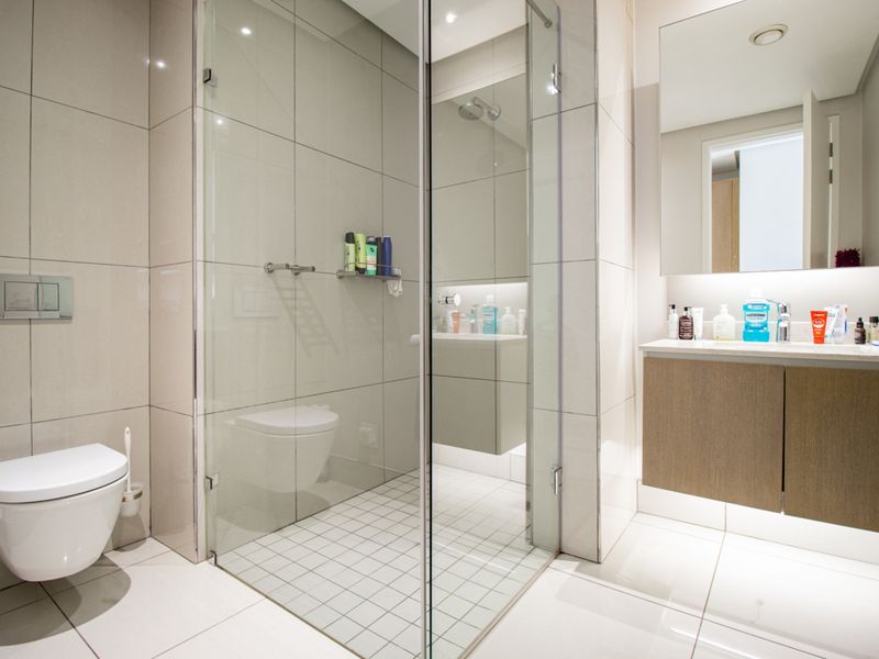 Modern bathroom featuring a wall-mounted toilet, glass-enclosed shower, and a sleek floating vanity with integrated under-cabinet lighting.