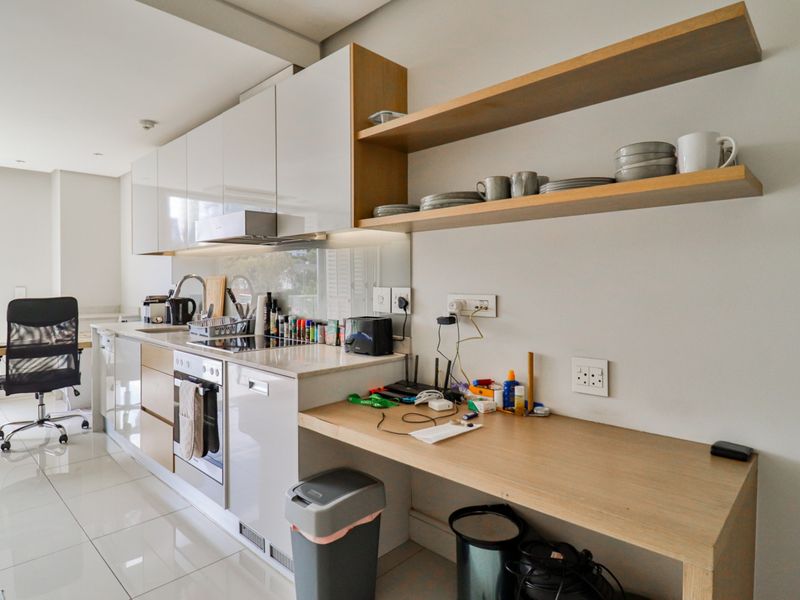 Modern kitchen featuring sleek high-gloss cabinetry, stone countertops, integrated oven, extractor fan, and open floating shelving with polished tiled flooring.