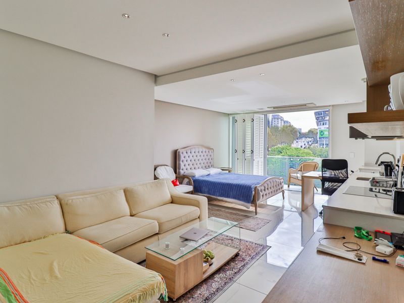 Modern open-plan apartment featuring a combined living and bedroom area, integrated kitchen, and access to a private balcony with urban views.