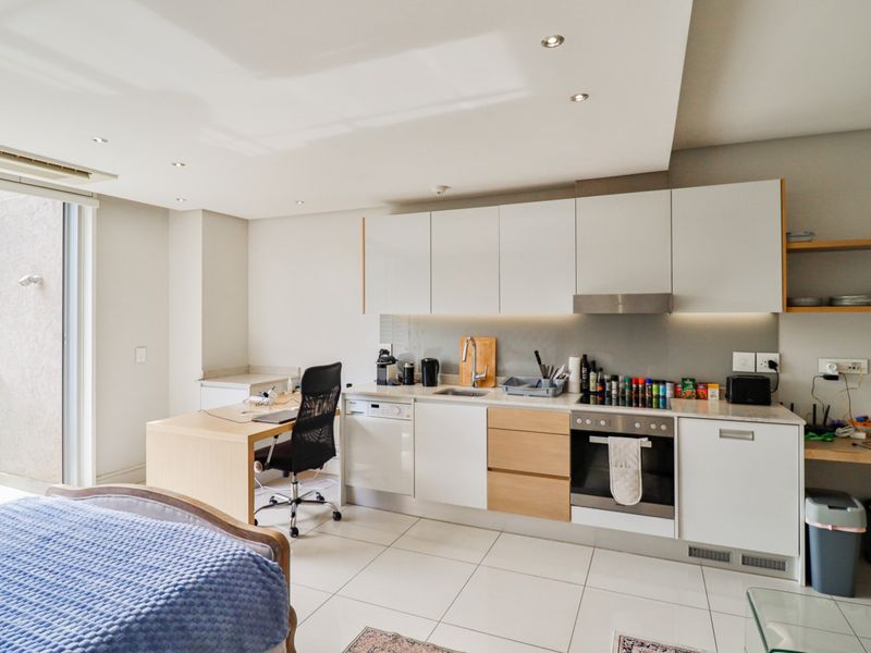 Modern open-plan kitchen featuring sleek cabinetry, integrated appliances, and tiled flooring, seamlessly connected to a bright living area with access to a balcony.