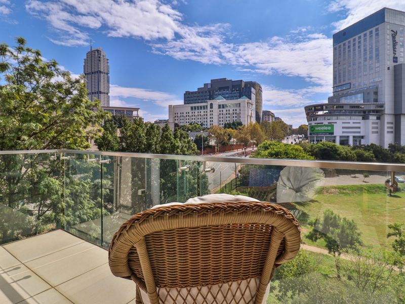 A modern balcony featuring a sleek glass balustrade with stainless steel fittings, offering an elevated urban view of the surrounding city skyline.