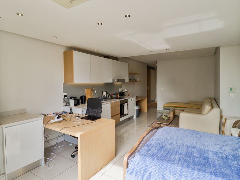 Open-plan apartment living area featuring a modern kitchen with built-in cabinetry, integrated appliances, and sleek tiled flooring throughout the space.
