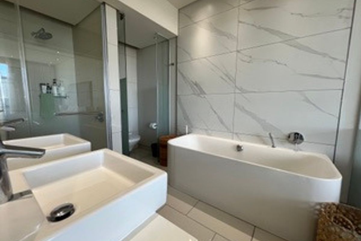 Modern bathroom featuring a sleek freestanding bathtub, double vanity, and a spacious glass-enclosed shower with contemporary marble-look wall tiling.