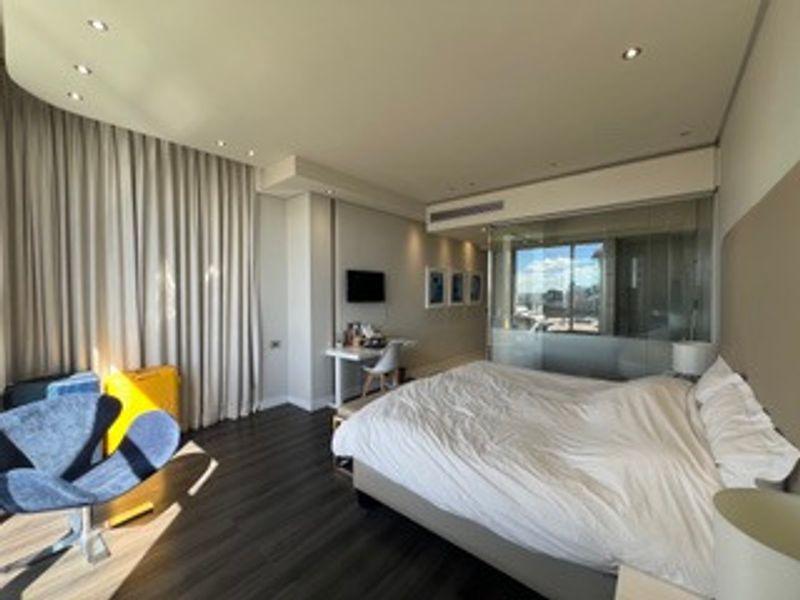 Modern bedroom featuring dark flooring, recessed lighting, ducted air conditioning, and a glass partition wall providing an open, contemporary feel.