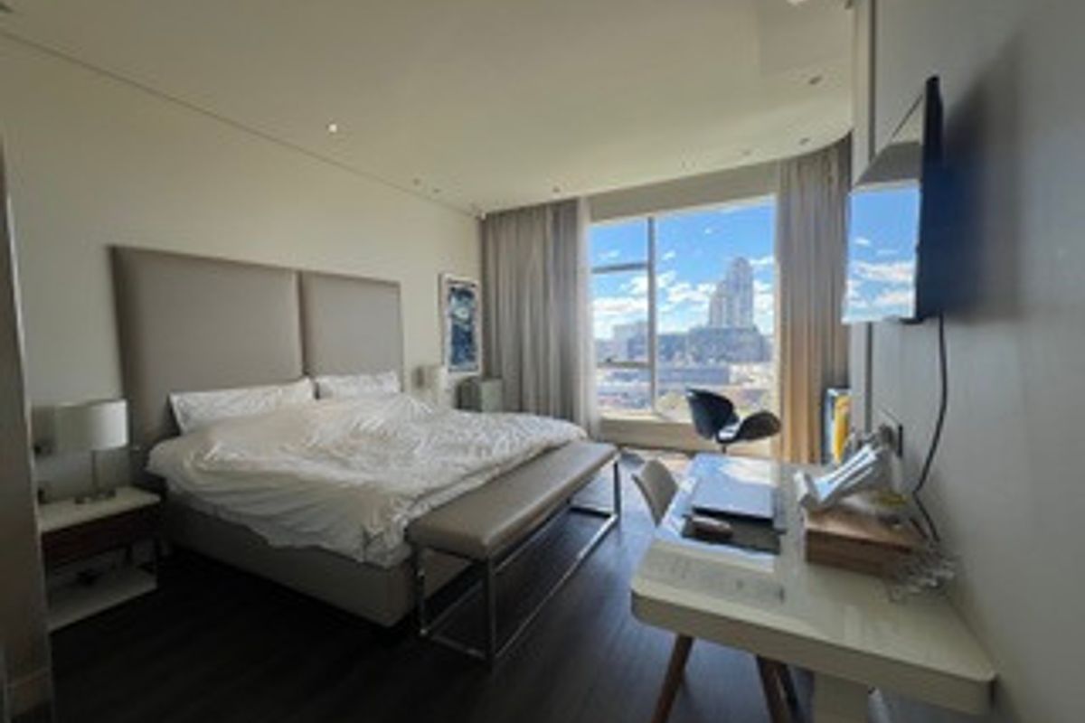 A modern bedroom featuring laminate flooring, recessed lighting, and a large window offering expansive city views.