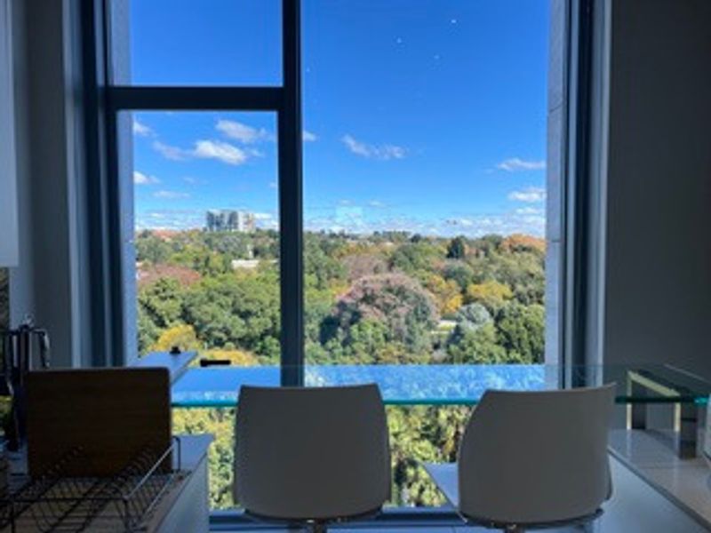 A bright interior space featuring a large floor-to-ceiling window that offers an expansive, scenic view of the surrounding greenery and cityscape.