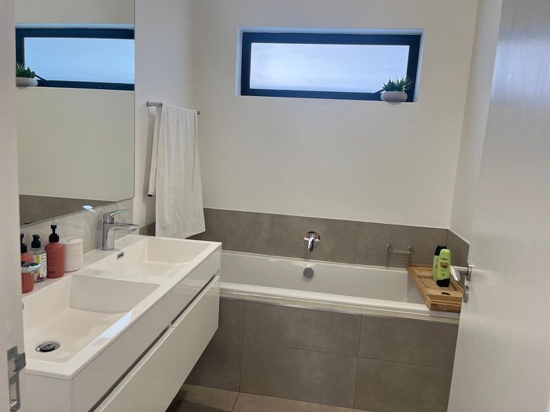 Modern bathroom featuring a sleek double vanity, large mirror, and a tiled built-in bathtub with contemporary fixtures.