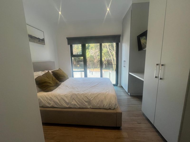 A modern bedroom featuring laminate flooring, built-in cupboards with a desk area, and a sliding glass door providing natural light and garden views.