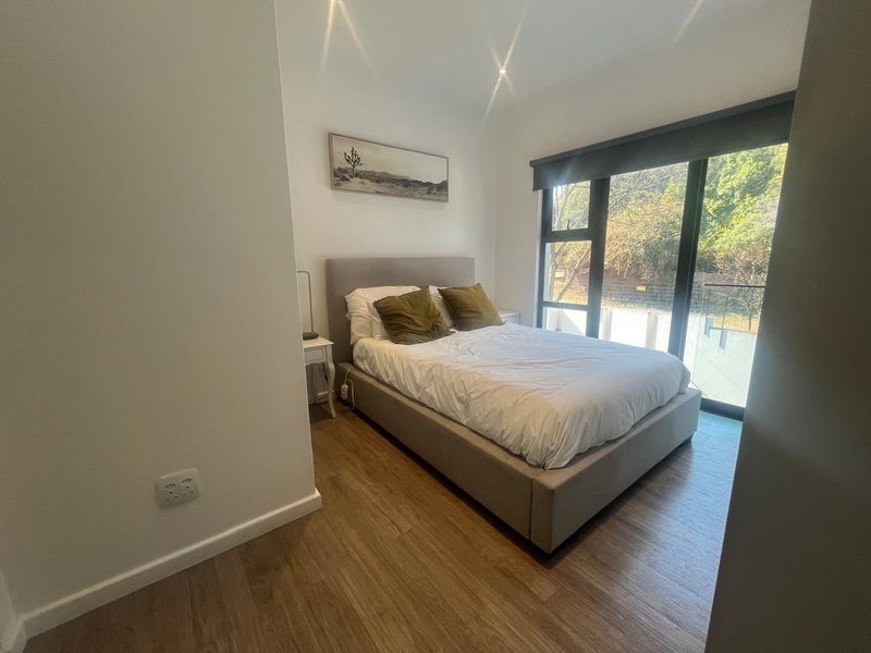A well-maintained bedroom featuring modern laminate flooring, recessed lighting, and a large sliding glass door providing natural light and outdoor access.
