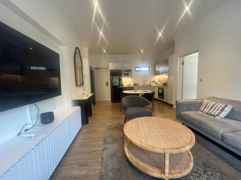 Open-plan living area featuring a modern kitchen with built-in cabinetry and integrated appliances, flowing into a comfortable lounge space with recessed lighting.