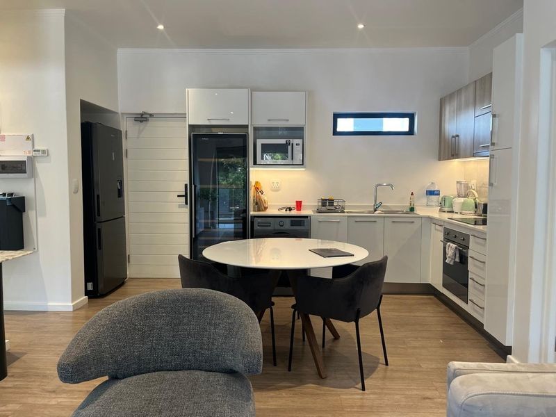 Modern open-plan kitchen featuring sleek white cabinetry, integrated appliances, and wood-look flooring, creating a functional and contemporary living space.