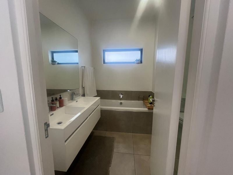 Modern bathroom featuring a double vanity, large wall-mounted mirror, and a tiled built-in bathtub with a horizontal window for natural light.