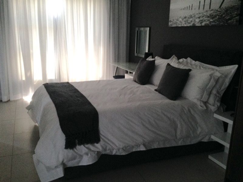 A well-lit bedroom featuring neutral tiled flooring and floor-to-ceiling sheer curtains, creating a bright and comfortable living space.