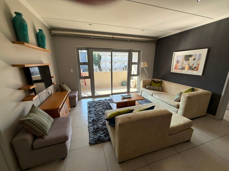 A well-lit living room featuring tiled flooring, recessed ceiling lighting, and a sliding glass door providing access to an outdoor balcony area.