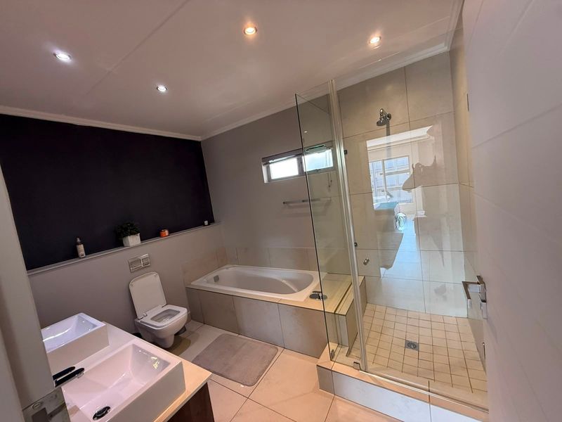 Modern bathroom featuring a double vanity, built-in bathtub, and a separate glass-enclosed shower with neutral tiling and contemporary finishes.