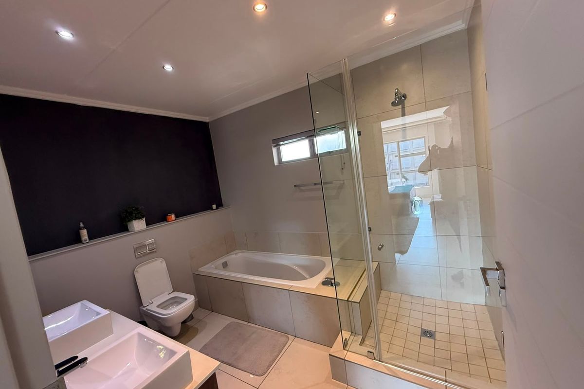 Modern bathroom featuring a double vanity, built-in bathtub, and a separate glass-enclosed shower with neutral tiling and contemporary finishes.