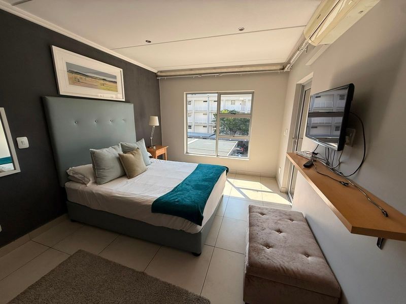A well-lit bedroom featuring tiled flooring, a wall-mounted air conditioning unit, and a floating shelf, offering a comfortable and functional living space.