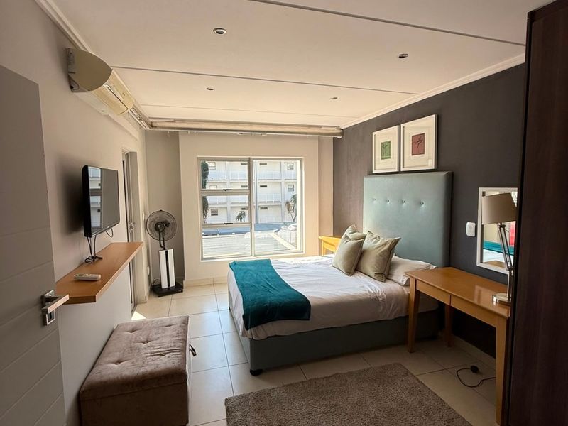 A well-maintained bedroom featuring tiled flooring, recessed ceiling lighting, an integrated air conditioning unit, and a large window providing natural light.
