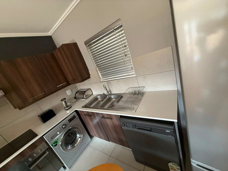 A functional kitchen featuring dark wood cabinetry, a double sink, tiled backsplash, and built-in appliances including an oven and hob.