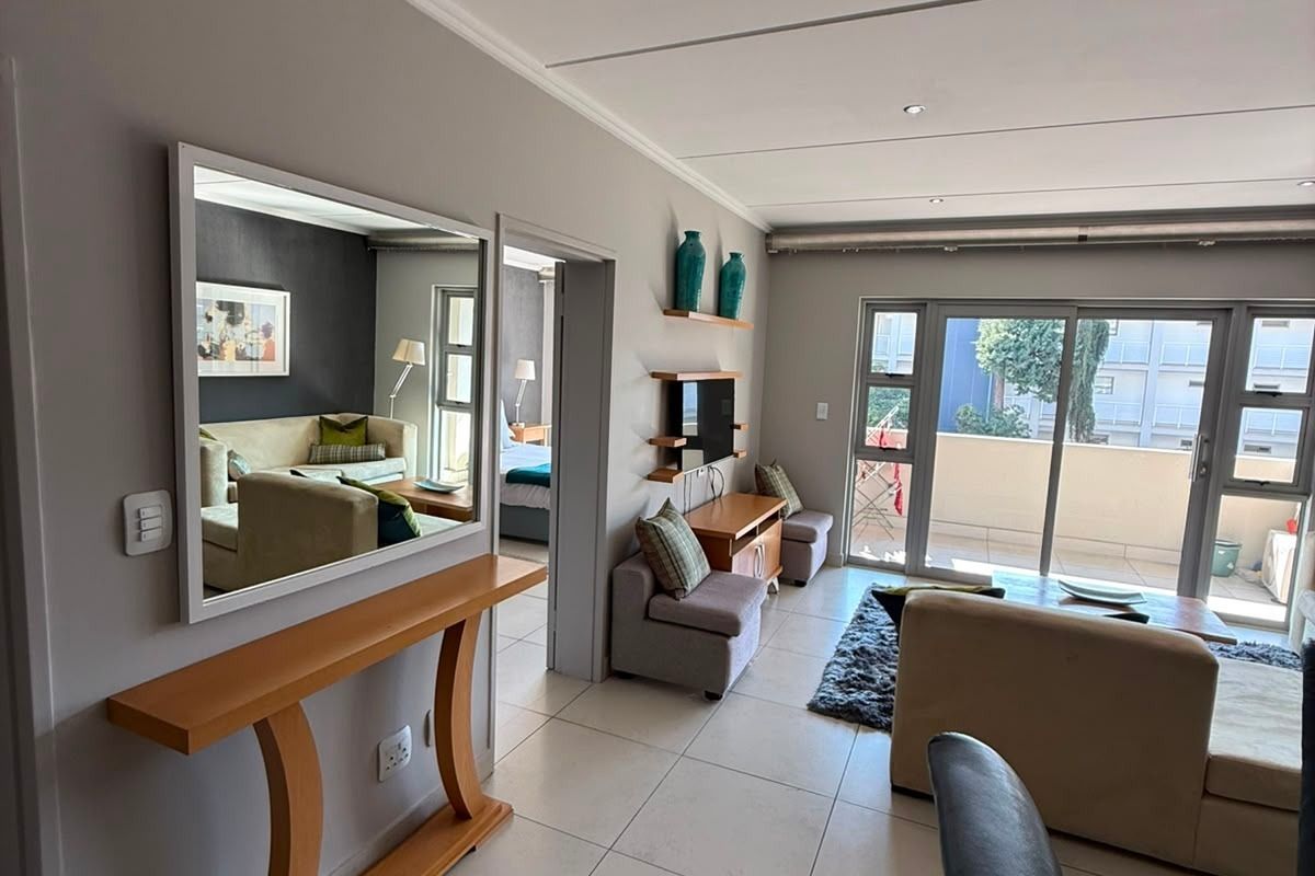 A bright, open-plan living area featuring large sliding glass doors leading to a balcony, neutral tiled flooring, and recessed ceiling lighting.