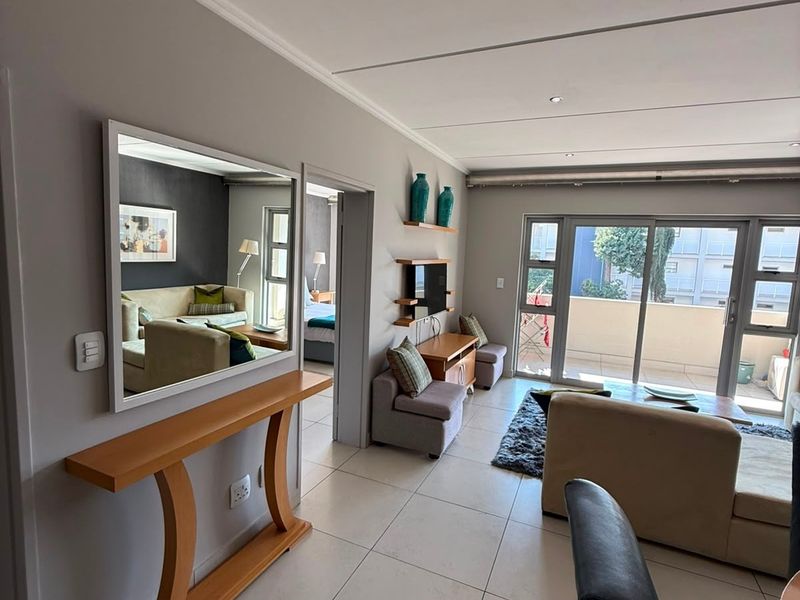 A bright, open-plan living area featuring large sliding glass doors leading to a balcony, neutral tiled flooring, and recessed ceiling lighting.