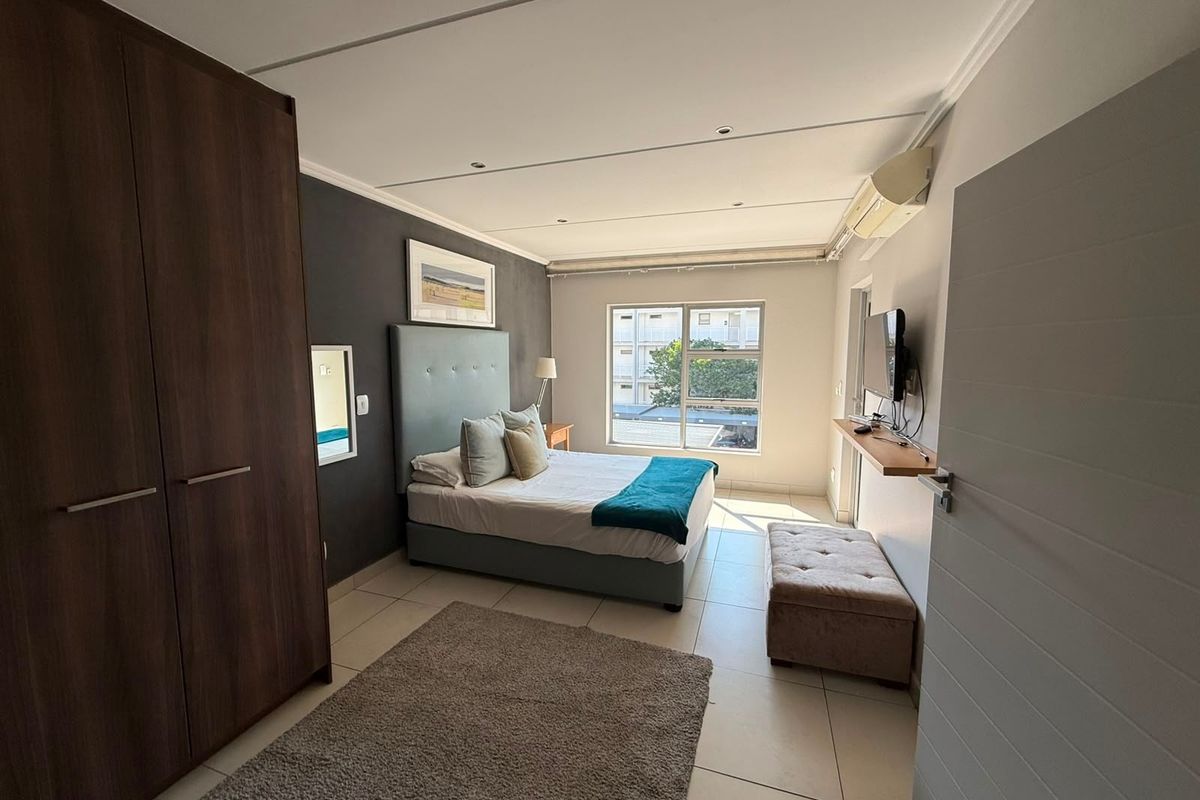 A well-maintained bedroom featuring tiled flooring, a built-in wardrobe, and a wall-mounted split-system air conditioner.