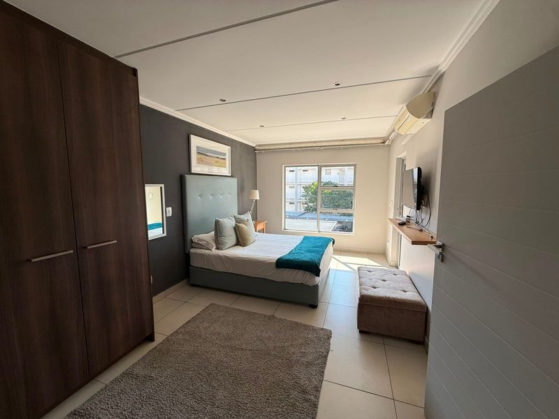 A well-maintained bedroom featuring tiled flooring, a built-in wardrobe, and a wall-mounted split-system air conditioner.