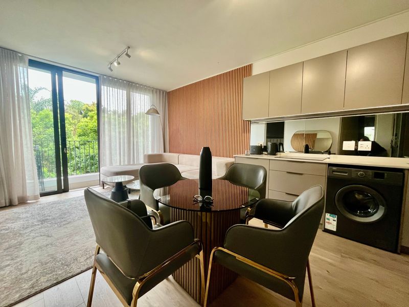 Modern open-plan living area featuring sleek built-in kitchen cabinetry, integrated laundry, stylish slatted wood wall accents, and large sliding doors leading to a balcony.