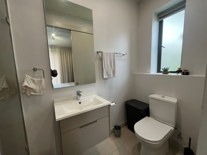A modern, well-maintained bathroom featuring a vanity cabinet with a basin, a wall-mounted mirror, a toilet, and a frosted glass window for natural light.