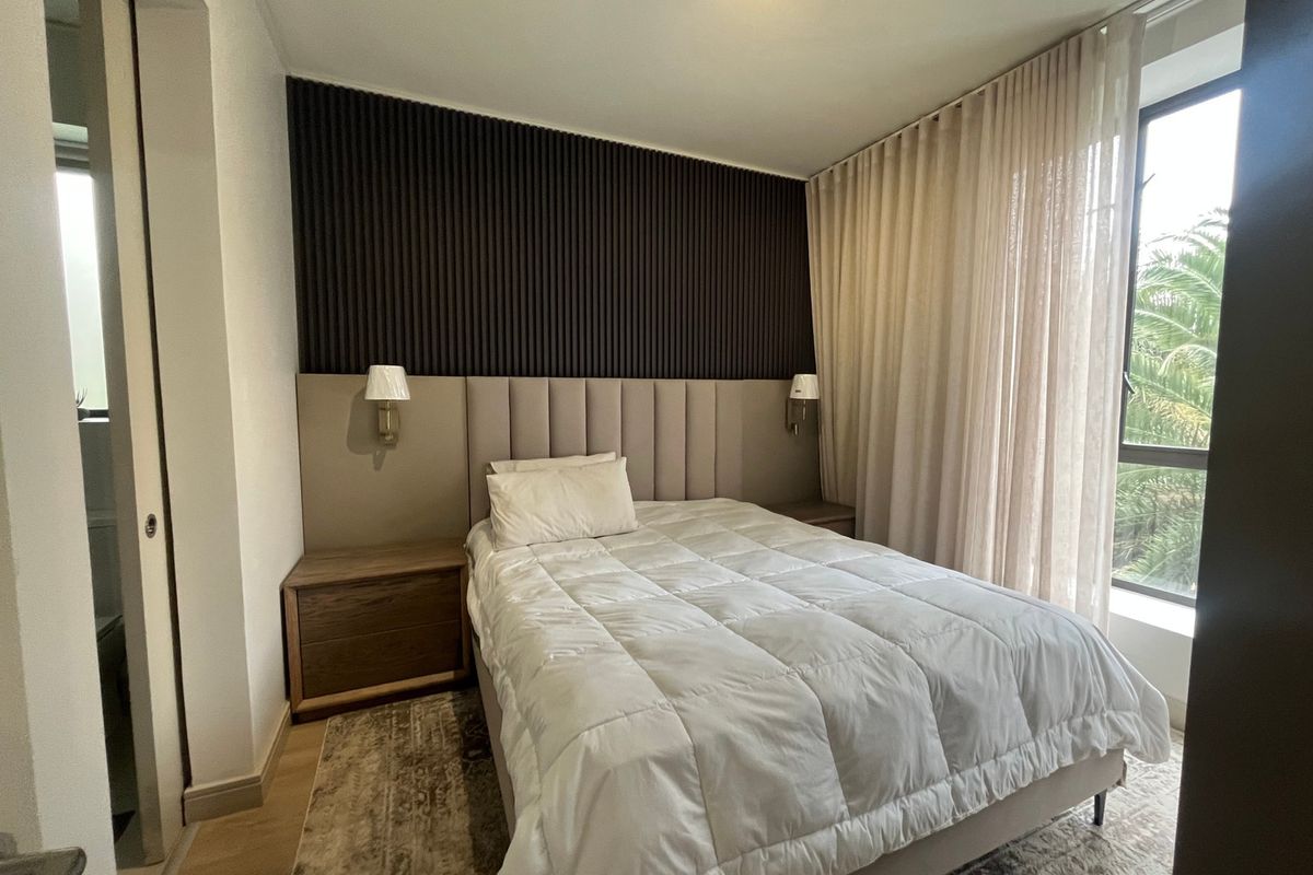 Modern bedroom featuring a stylish slatted feature wall, integrated upholstered headboard, wall-mounted lighting, and large windows with floor-to-ceiling curtains.