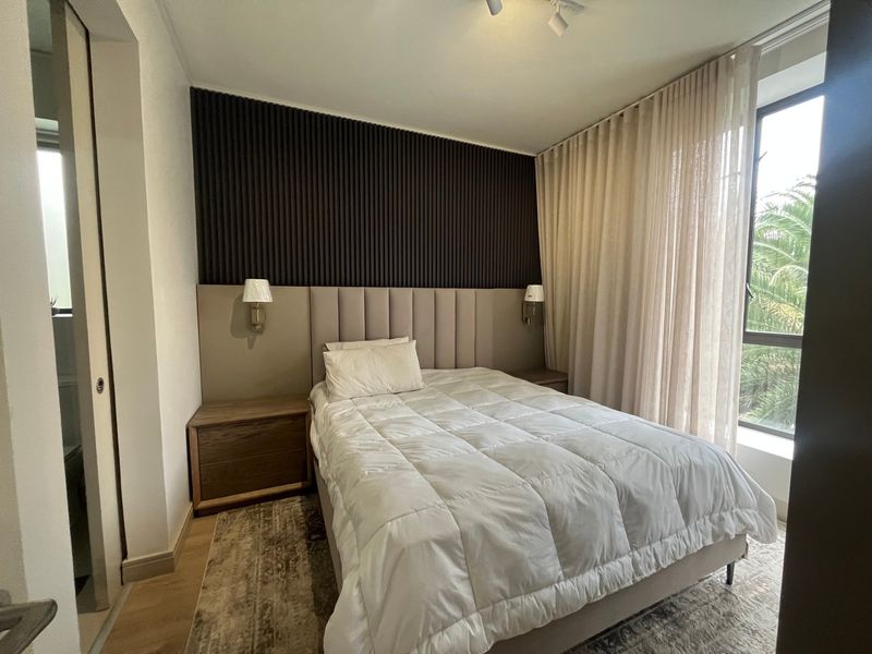 Modern bedroom featuring a stylish slatted feature wall, integrated upholstered headboard, wall-mounted lighting, and large windows with floor-to-ceiling curtains.