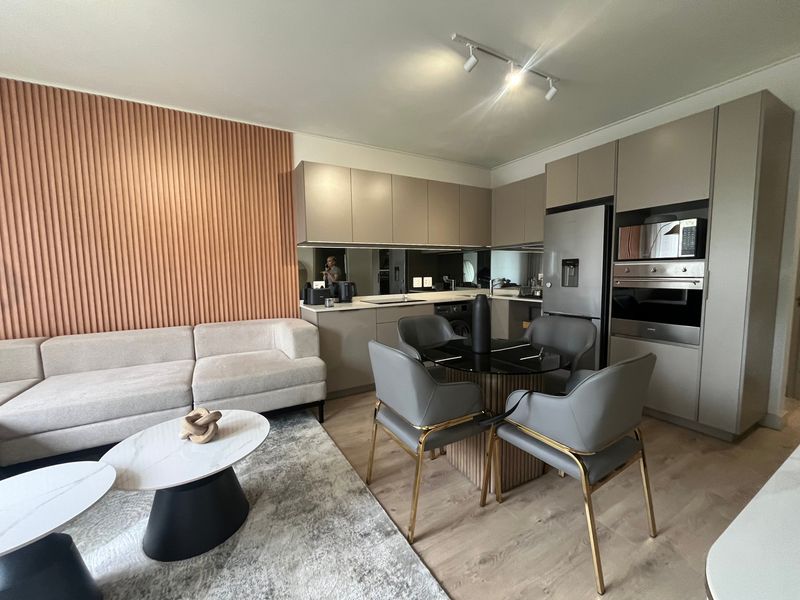 Modern open-plan living and kitchen area featuring sleek cabinetry, integrated appliances, a stylish mirror splashback, and contemporary slatted wall detailing.