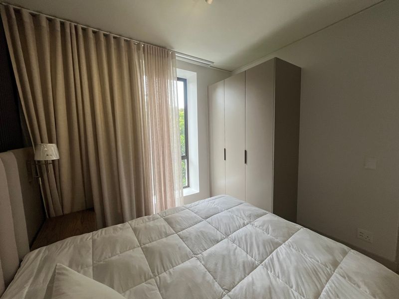 A well-maintained bedroom featuring a built-in wardrobe, neutral wall finishes, and a recessed window with floor-to-ceiling curtains.