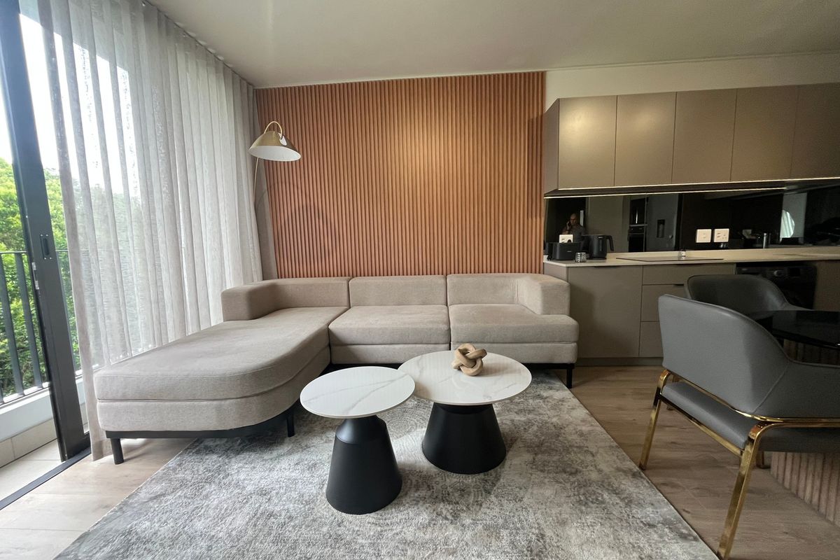 Modern open-plan living area featuring contemporary kitchen cabinetry, stylish slatted timber wall accents, and seamless access to a private balcony through sliding glass doors.