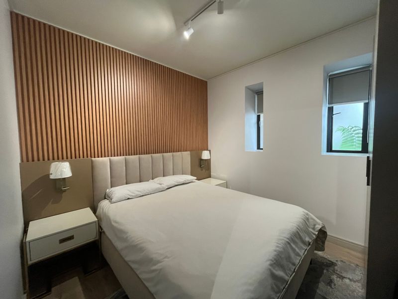 A modern bedroom featuring a stylish slatted timber accent wall, recessed windows, and contemporary track lighting.