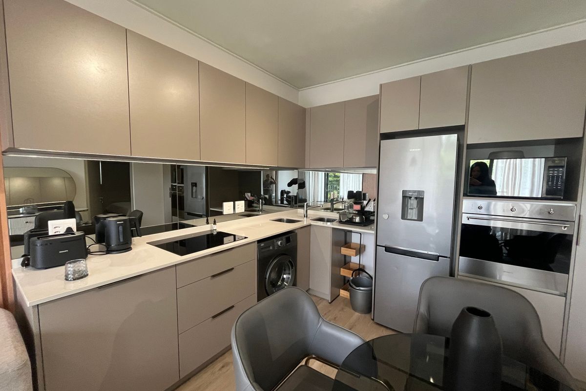 Modern kitchen featuring sleek handleless cabinetry, stone countertops, a mirrored splashback, and integrated appliances including an oven, microwave, and washing machine.