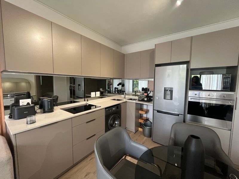 Modern kitchen featuring sleek handleless cabinetry, stone countertops, a mirrored splashback, and integrated appliances including an oven, microwave, and washing machine.