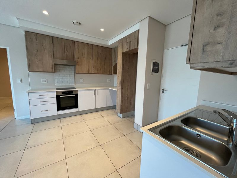 Modern kitchen featuring wood-tone and white cabinetry, built-in oven and hob, subway tile backsplash, and double sink with tiled flooring.