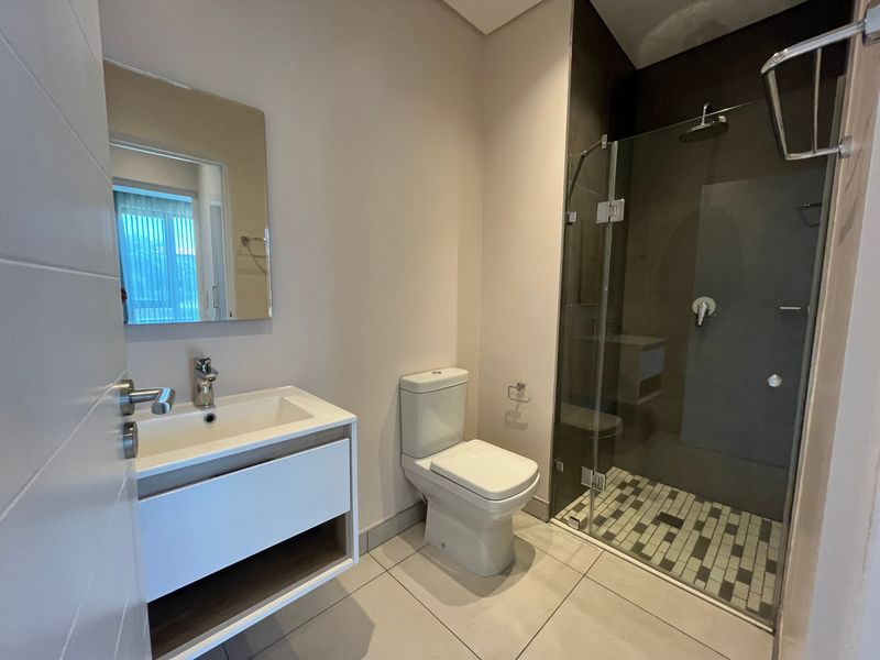 Modern bathroom featuring a sleek vanity with basin, a wall-mounted mirror, a toilet, and a glass-enclosed shower with contemporary tiling.